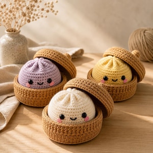 Puede incluir: Tres peluches de ganchillo con forma de bollos al vapor, cada uno en una cesta de ganchillo color canela con tapa a juego. Los bollos son de color lavanda, amarillo y blanco, con ojos de cuentas negras, sonrisa bordada y mejillas rosadas.