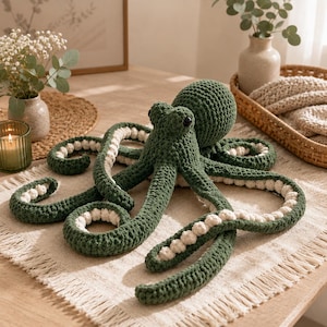 May include: A dark green crocheted octopus toy featuring a rounded head, two small black eyes, and eight long, curled tentacles. The underside of each tentacle is lined with a row of small, cream-colored, circular crocheted bobble accents.