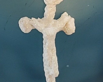 May include: A cream-colored, cross-shaped pendant with glitter accents hangs from a matching rope. The cross has rounded edges and a textured surface. The background is a solid teal color.