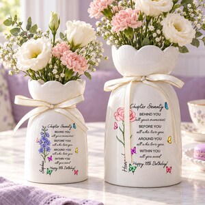 May include: Two white ceramic vases with scalloped rims, each tied with a cream ribbon. The vases feature floral illustrations, colorful butterflies, and the printed text: Chapter Seventy, BEHIND YOU all your memories, BEFORE YOU all who love you, AROUND YOU all who love you, WITHIN YOU all you need, Happy 70th Birthday!