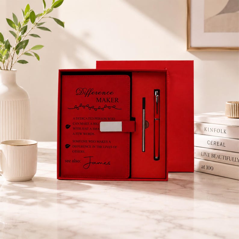 Pu&ograve; includere: Una scatola regalo rettangolare rossa contenente un taccuino rosso con chiusura magnetica argentata e una penna rossa abbinata. La copertina del taccuino presenta il testo nero Difference MAKER, una definizione e il nome James in basso.