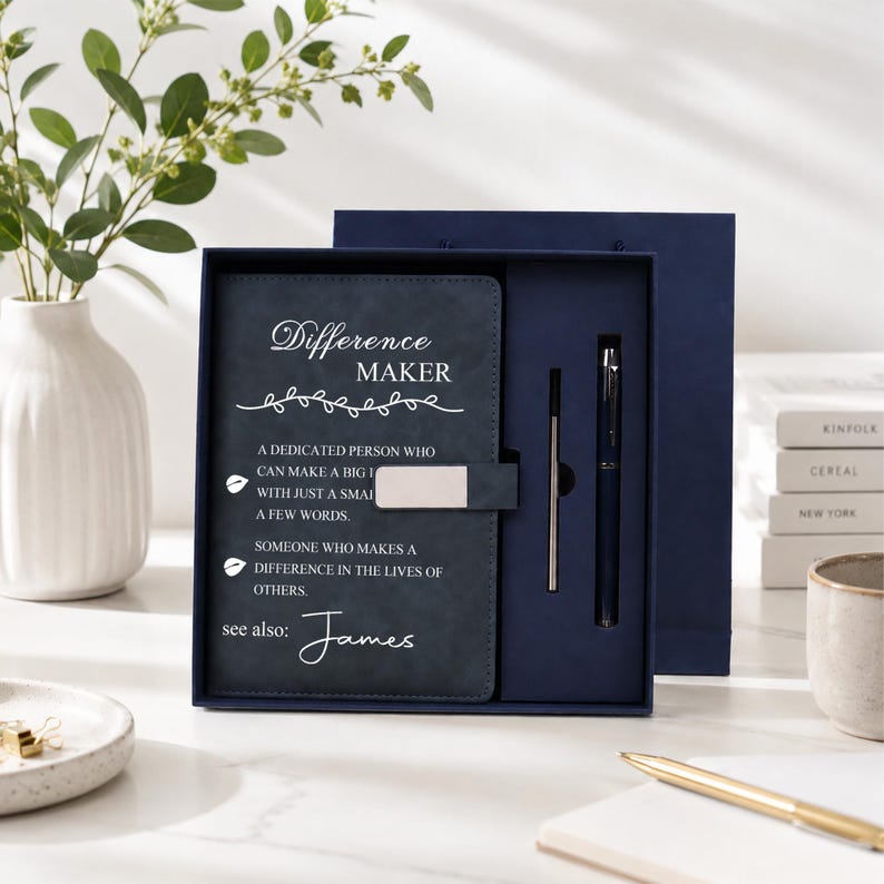 Pu&ograve; includere: Un set regalo blu scuro contenente un taccuino con chiusura magnetica argentata e una penna abbinata. La copertina del taccuino riporta il testo "Difference MAKER" e una definizione, con il nome "James" stampato nella parte inferiore.
