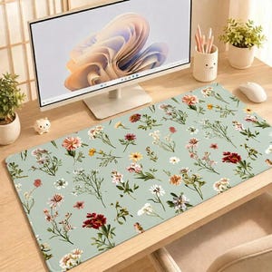 Peut inclure: Un grand tapis de bureau rectangulaire avec un fond vert sauge clair orné d'un motif répétitif de fleurs sauvages dans des tons de rouge, rose, jaune et blanc, posé sur un bureau en bois devant un écran d'ordinateur.