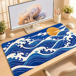 May include: A rectangular desk mat featuring a stylized graphic of deep blue ocean waves with white foam crests and a large, solid gold circular sun set against a dark blue background, laid flat on a wooden desk surface.