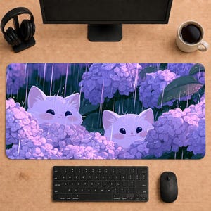 May include: A rectangular desk mat featuring a digital illustration of two white kittens peeking out from clusters of purple hydrangea flowers during a rain shower. The scene includes vertical rain streaks and green leaves among the blossoms.
