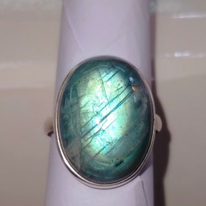 May include: A silver ring with a large oval-shaped blue labradorite gemstone. The stone has a shimmering iridescent effect.