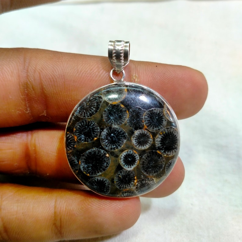 May include: A silver pendant featuring a round, black and white fossilized stone with a circular pattern. The pendant is on a silver chain.