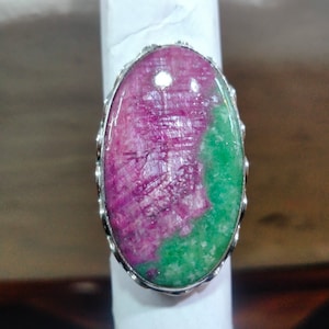 May include: A silver ring with a large oval-shaped gemstone. The gemstone is a mix of pink and green, with a swirling pattern.