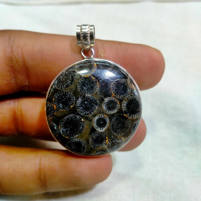 May include: A silver pendant featuring a round, black and white fossilized coral stone with a circular pattern.