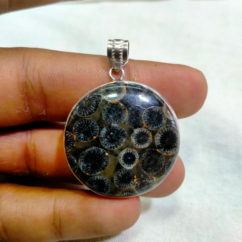 May include: A silver pendant featuring a round, black and white fossilized stone with a circular pattern. The pendant is on a silver chain.