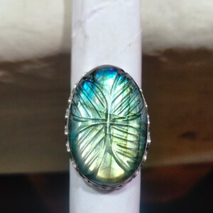 Könnte beinhalten: Ein silberner Ring mit einem großen ovalen, blauen und grünen Labradorit-Edelstein. Der Edelstein hat ein geschnitztes Design.