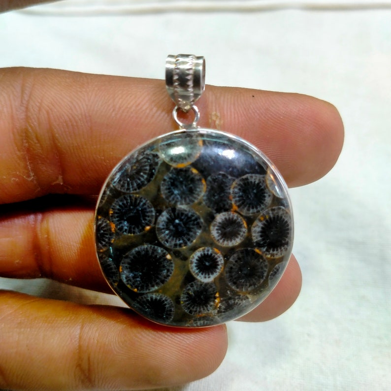 May include: A silver pendant with a round, black and white fossilized coral stone. The stone has a circular pattern.