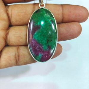 May include: Oval pendant with a green and purple stone set in a silver-colored metal frame. The pendant hangs from a thin, silver-colored chain. The stone has a polished, glossy finish.