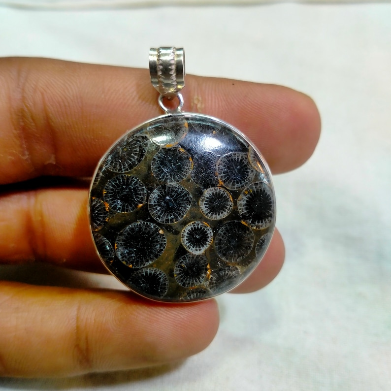 May include: A silver pendant with a round black and white fossilized coral stone. The stone has a circular pattern.