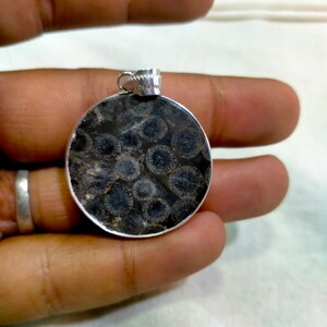 May include: A round silver pendant with a black fossilized coral design. The pendant is approximately 1 inch in diameter.