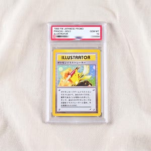 Puede incluir: Una carta Pokémon Pikachu Illustrator promocional japonesa de 1998, encapsulada en una funda protectora transparente. La carta muestra un Pikachu amarillo sosteniendo un pincel, con el texto ILLUSTRATOR y caracteres japoneses impresos.