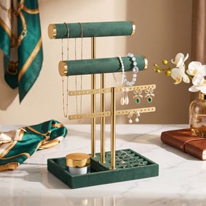 May include: A multi-tiered jewelry organizer featuring two dark green velvet-covered horizontal bars and two gold-toned metal earring racks. The base is a dark green velvet tray with a gold-capped container and several silver rings.