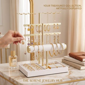 May include: A gold-toned metal jewelry stand with a white base and a white cylindrical bar for bracelets. The stand features multiple hooks for necklaces and perforated bars for earrings. Text reads: YOUR TREASURED COLLECTION, ARTFULLY DISPLAYED.