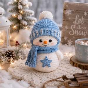 May include: A crocheted snowman figurine featuring a white round body with a blue star appliqué, wearing a light blue knit hat with a white pom-pom and a matching blue scarf. The snowman has black bead eyes, a small orange nose, and pink cheeks.