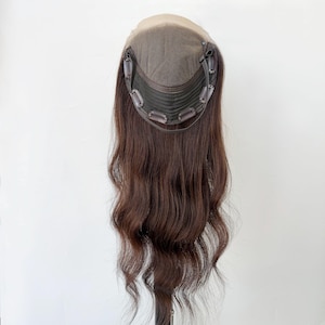 Peut inclure: Un postiche capillaire long et ondulé de couleur brune, doté d'une base en dentelle beige et d'un intérieur en maille marron foncé. Le dessous de la pièce comprend plusieurs petites pinces métalliques fixées sur le pourtour.