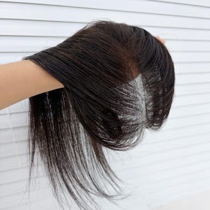 May include: A dark brown hair topper featuring a monofilament base with a visible center part. The hair is straight, smooth, and sleek, with a natural-looking scalp appearance at the parting area, designed to provide coverage and volume.