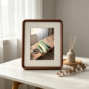 May include: A rectangular wooden picture frame with a white mat board containing a photograph of three light green and white squash resting on a wooden surface next to a pair of black scissors. The frame has rounded corners and a dark brown finish.