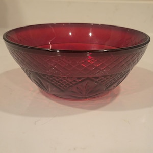 Puede incluir: Un cuenco de cristal rojo intenso con un exterior texturizado que presenta un patrón de rombos en la parte superior y una serie de motivos en forma de abanico prensados alrededor de la base, creando un aspecto facetado con borde liso.
