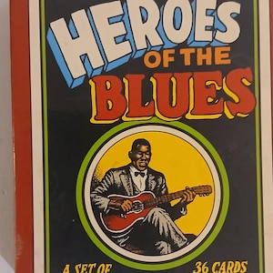 May include: A rectangular box set titled Heroes of the Blues containing 36 cards. The cover features a black and white illustration of a musician playing a guitar inside a yellow circle, with text by Stephen Calt and art by R. Crumb.
