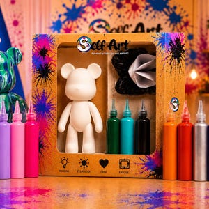 May include: A Self Art DIY kit featuring a white bear figurine, a black and white paper accessory, and fourteen squeeze bottles of colorful paint. The cardboard box displays the Self Art logo and text including Imagine, Eclate toi, Cree, and Expose.