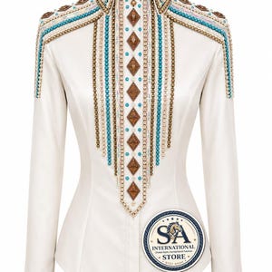 May include: A cream-colored long-sleeve shirt featuring a high collar, embellished with vertical rows of brown diamond-shaped stones, turquoise beads, and metallic gold chains. The shoulders and cuffs are decorated with matching beadwork.