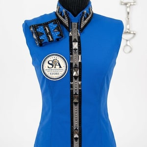 May include: A bright blue sleeveless show shirt featuring a high collar with black and silver geometric trim, a vertical center panel adorned with metallic studs and crystals, and a matching cuff. A circular logo reads SA INTERNATIONAL STORE.