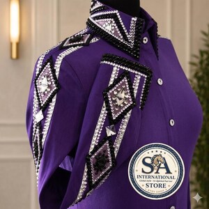 Può includere: Una camicia a maniche lunghe color viola vivace con colletto strutturato e pannelli sulle spalle decorati con intricati motivi a rombi realizzati con cristalli neri e trasparenti. Il capo presenta una chiusura frontale a bottoni e un logo circolare.