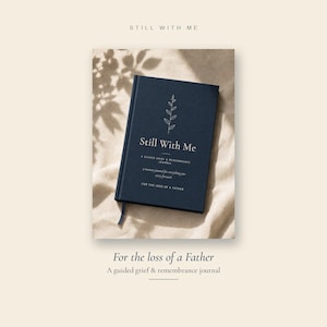 Op de afbeelding: Een donkerblauw notitieboek met harde kaft en een witte lijntekening van een takje op de omslag. De tekst luidt Still With Me, A Guided Grief & Remembrance Journal, a memory journal for everything you carry forward, For the loss of a Father.