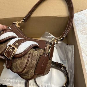 These are the Coach Ashton Shoulder Bags in signature jacquard and smooth leather, featuring distinctive front buckle pockets and detachable straps.