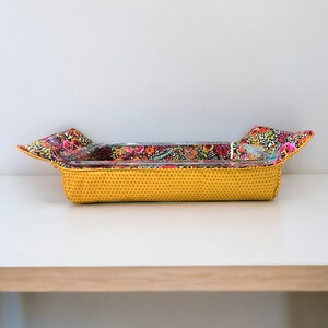 May include: A yellow fabric baking dish liner with a floral print. The liner has a glass baking dish inside.