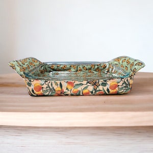 May include: A green and yellow fabric-covered baking dish with a glass interior. The fabric features a pattern of butterflies and oranges.