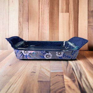 May include: A blue and gray fabric-covered baking dish with a floral pattern. The dish is sitting on a wooden surface.
