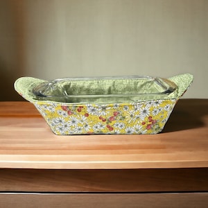 May include: A yellow and green floral fabric casserole dish carrier with a glass baking dish inside.