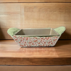 May include: A floral patterned fabric loaf pan liner with a metal loaf pan inside. The liner has a green polka dot trim.