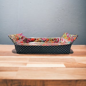 Può includere: Una teglia da forno rivestita in tessuto a pois neri e bianchi con una fodera a stampa floreale. La teglia è vuota e si trova su una superficie in legno.