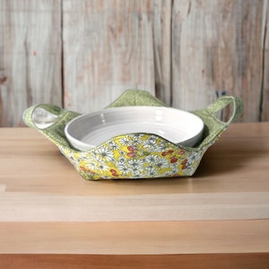 Puede incluir: Un bol de tela verde con un patrón floral en amarillo, blanco y rojo. El bol contiene dos cuencos de cerámica blanca.