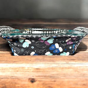 May include: A black and white checkered fabric casserole dish holder with a blue and white mitten pattern. The holder is quilted and has a black background.