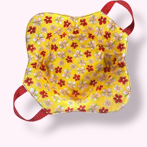 Puede incluir: Un protector de cuenco amarillo con un estampado floral de flores rojas y rosas. El protector tiene asas rojas con lunares blancos. El interior también es amarillo con el mismo diseño floral.