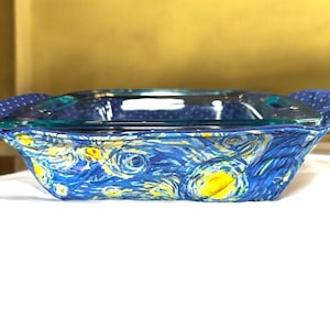 Puede incluir: Un portador de fuente para horno acolchado azul y amarillo con un diseño de noche estrellada. El portador está hecho de tela y tiene asas a cada lado.