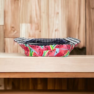 Puede incluir: Un porta platos de tela con estampado de sandía y forro de cuadros negros y blancos. El porta platos está vacío y se encuentra sobre una superficie de madera.