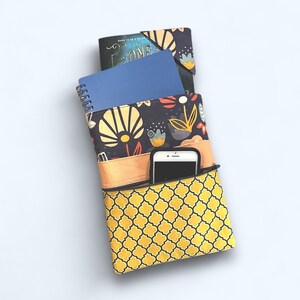 May include: A black and yellow fabric pouch with a floral pattern and a phone pocket. The pouch has a blue notebook and a book with the title "Born to be a Malfoy" inside.