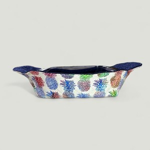 May include: A white quilted casserole dish with blue handles and a pineapple print. The pineapples are in shades of blue, green, red, and purple.