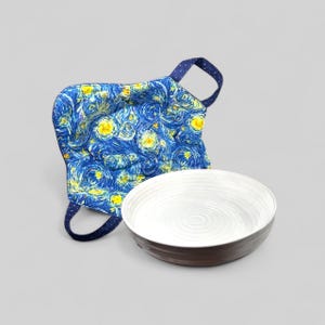May include: A blue oven mitt with a starry night design and a white ceramic bowl with a brown rim. The oven mitt has a dark blue polka dot handle. The bowl has a white interior with concentric circles.