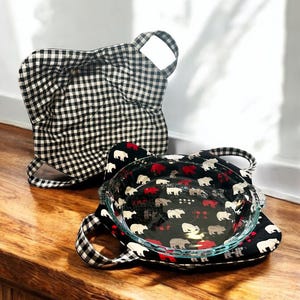 May include: Two black and white checkered fabric hot pads. One hot pad is folded and the other is holding a clear glass pie plate with a black and white print of red and gray bears.