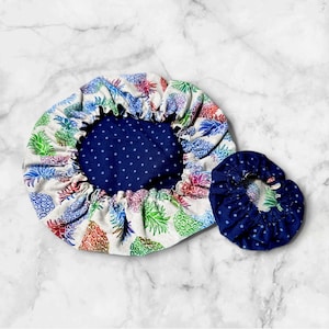 Op de afbeelding: Twee herbruikbare voedselhoezen, een met een blauw-wit stippenpatroon en de andere met een witte achtergrond en een kleurrijke ananasprint.